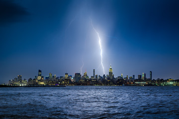 Wall Mural - Lightning striking New York City skyscrapers at night. Stormy skies over Midtown Manhattan from the Hudson River