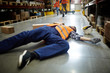 Fallen worker lying on the floor in aisle between storage shelves