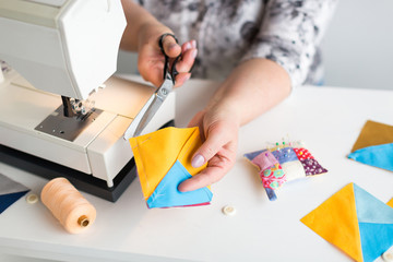 Wall Mural - patchwork and quilting in the workshop of a tailor woman on white background - close-up on hands of a tailor woman at work with scissors and colorful stitched in fabric