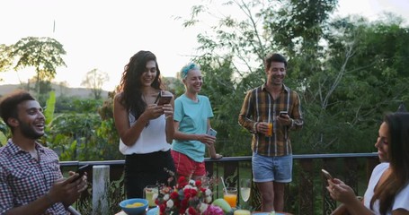 Wall Mural - People Group Use Cell Smart Phones Talking Sitting At Table Outdoors On Terrace Young Friends Happy Smiling Social Media Communication Slow Motion 60