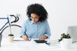© wayhome.studio  - Portrait of attractive hardworking businesswoman with Afro hairstyle busy doing paperwork at office desk, working through finances, using calculator and making notes in her notebook with pen