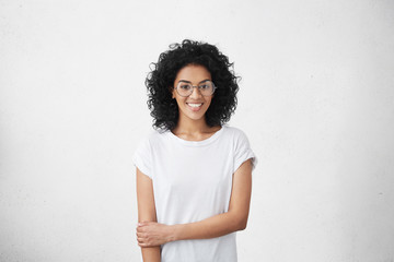 Wall Mural - Relaxed carefree smiling young woman wearing white t-shirt and glasses having positive cheerful expression on her face, rejoicing at her leisure time, spending day at home. Horizontal studio shot