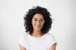 Leinwandbild Motiv Close up studio shot of beautiful young mixed race woman model with curly dark hair looking at camera with charming cute smile while posing against white blank copy space wall for your content