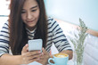 © Farknot Architect - Beautiful Asian girl with smiley face holding and using smart phone in modern pastel color cafe