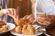 close up man hand holding smartphone talking with woman who try to eat fired chicken for lunch break.