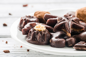 Raw homemade chocolate candies on a plate on white wooden background. Healthy vegan sweets. Close up