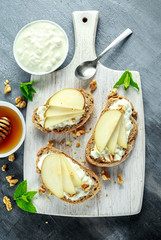 Wall Mural - Appetizer bruschetta with pear, honey, walnut and cottage cheese on white board.