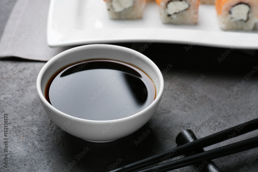 Bowl with tasty soy sauce on grey textured background
