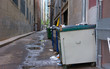 Dirty filthy back alley with dumpsters, old trash, awful puddles filled with a brine of garbage leakage and toxic chemicals