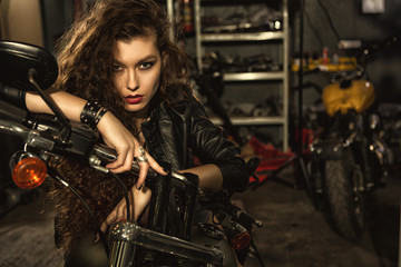 Beautiful young biker woman on her motorcycle at the workshop