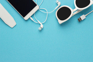 Poster - studio shot of white sunglasses smart phone and earbuds on blue background