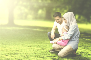 Wall Mural - Muslim parents squatting with baby in meadow