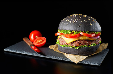 Wall Mural - Black burger with tomatoes isolated on black background. 