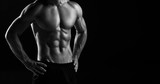 Fototapeta  - The torso of attractive male body builder on black background.