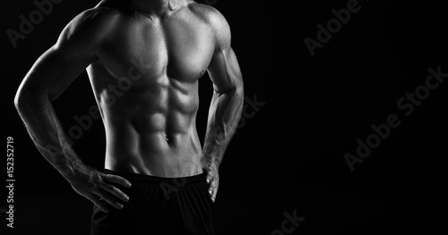 Fototapeta  The torso of attractive male body builder on black background.