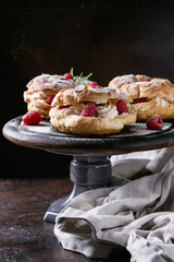 Homemade choux pastry cake Paris Brest with raspberries, almond and rosemary, served on black wooden serving board on cake stand over dark texture background. French dessert