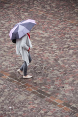 Wall Mural - femme marchant avec un parapluie sur un place pavée