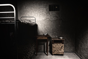 A dark empty prison cell with bunk bed and bedside table