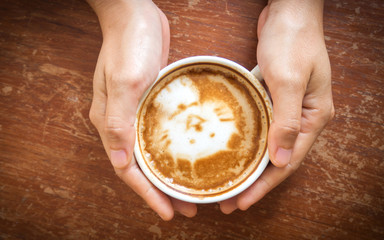 Wall Mural - Woman hands holding cup of coffee. Top view. Cute latte art, cat paint. With dark vignette.