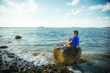 boy sitting on a rock by the sea. Child on the beach looking into the distance. Copy space for your text