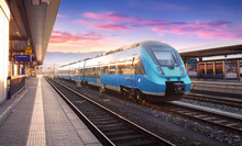 Beautiful View With Modern High Speed Train On The Railway Station And Colorful Sky With Clouds At Sunset In Europe. Industrial Landscape With Blue Train On Railway Platform. Railroad Background 