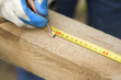 Dłoń pracownika budowlanego zaznacza ołówkiem odległość na drewnianej kantówce.