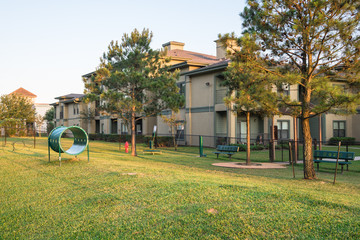 Wall Mural - Community on-site dog park at the grassy backyard of a typical apartment complex building in suburban area at Humble, Texas, US. Off-leash dog park with pet stations, toys and bag dispensers