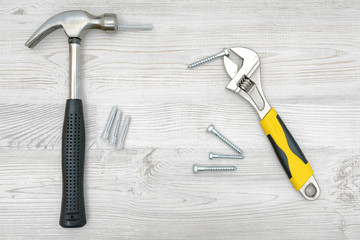 Wall Mural - A silver hammer, a wrench, several screw bolts and dowels on light wooden background.