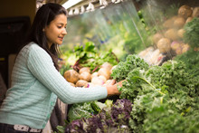 Closeup Portrait, Beautiful, Pretty Young Woman In Sweater Picking Up, Choosing Green Leafy Vegetables In Grocery Store