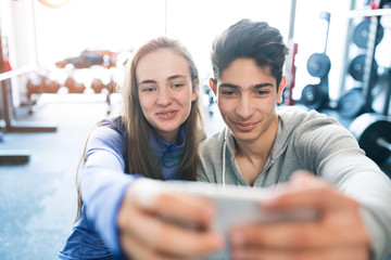 Wall Mural - Fit couple in modern crossfit gym with smartphone.