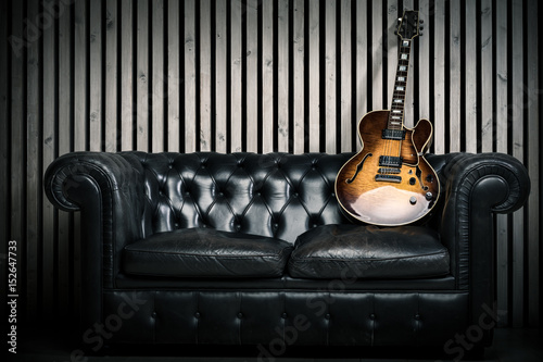 Zdjęcie XXL puste vintage sofa i gitara elektryczna z nowoczesnym tle ściany drewna studio nagrań. Muzyczny pojęcie z nikt