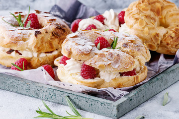 Homemade choux pastry cake Paris Brest with raspberries, almond, sugar powder and rosemary, served on wooden serving tray over gray blue texture background. French dessert. Close up