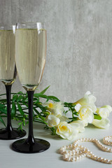 A bouquet of white freesia, two glasses of champagne and pearl necklace.