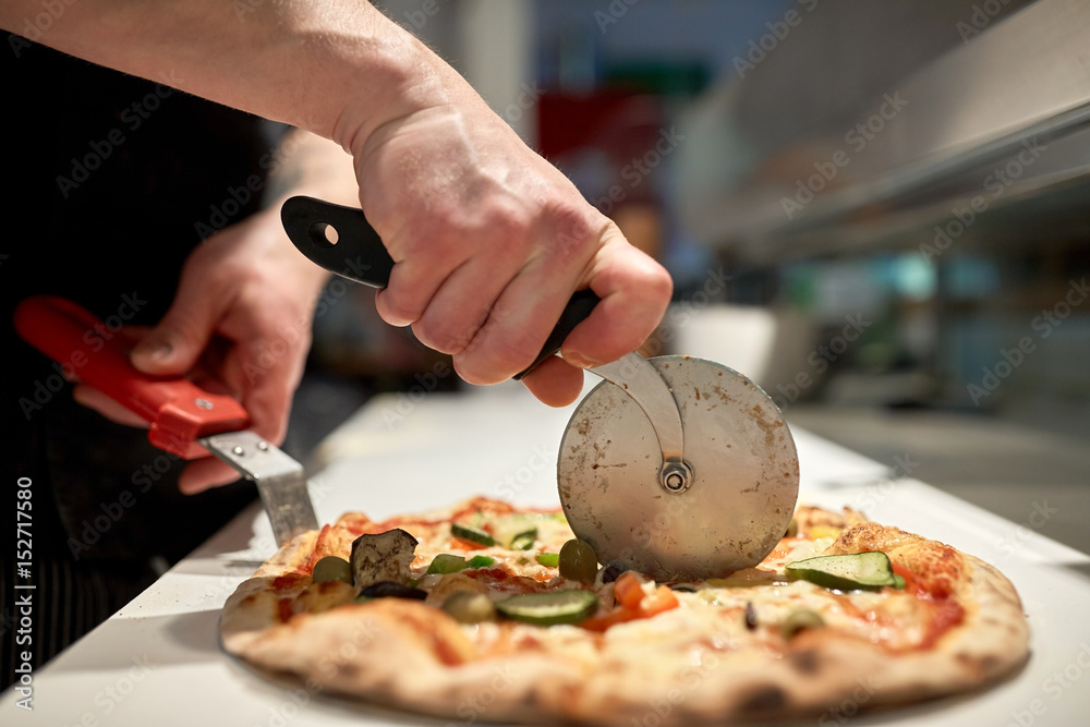 cook cutting pizza to pieces at pizzeria - obrazy, fototapety, plakaty 