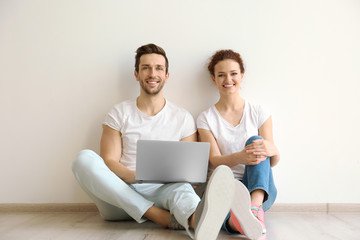 Wall Mural - Happy young couple with laptop sitting on floor at home