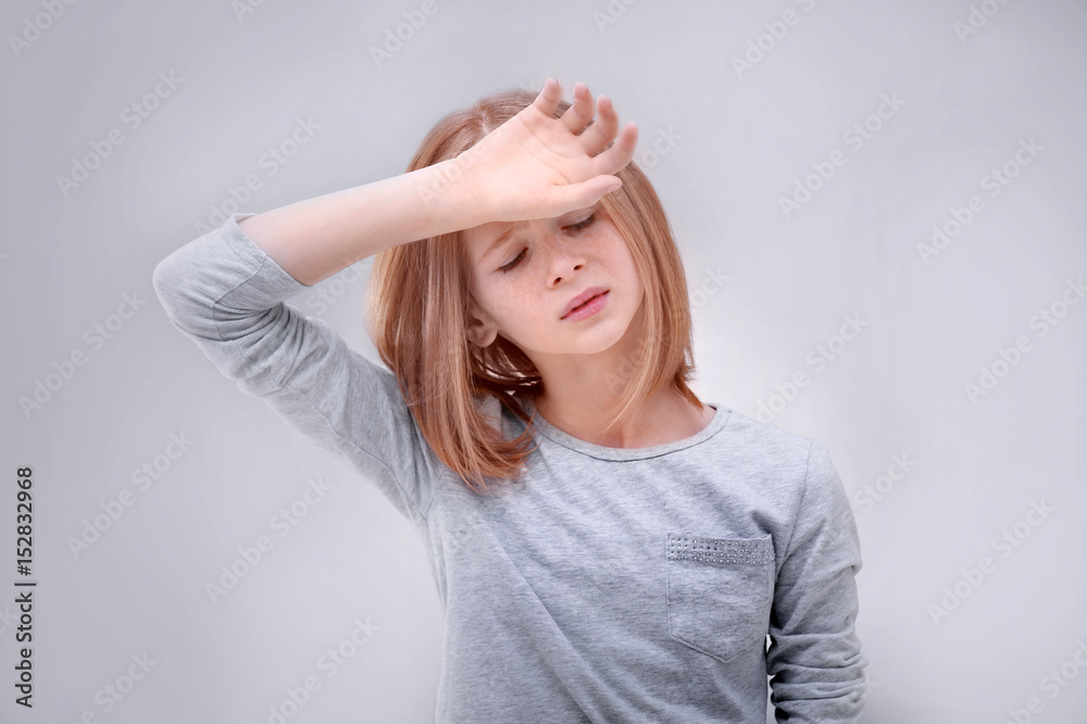 Cute girl suffering from headache on grey background