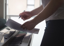 Musician Brainstorming And Innovating New Song Ideas At Piano By The Window. Composer Writing Notes To Paper Or Planning Arrangement. Man Come Up With Pop Lyrics. Inspiration And Creativity Concept.