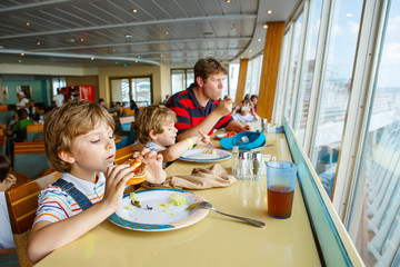 Two preschool kids boys and father eating hamburger sitting in cafe on cruise ship