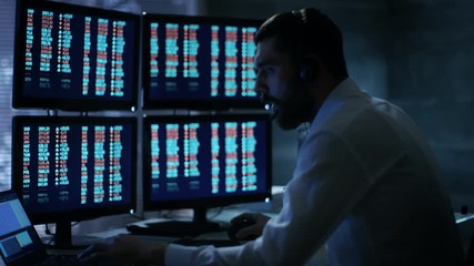 Aufkleber - Late at Night Trader Reads Numbers on His Multiple Displays with Stock Information on Them, He Also Consults Clients with Headset On. In Background Big City Window View. Shot on RED Cinema Camera 4K