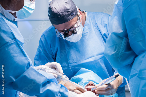 Fotomural A male dentist in uniform perform dental implantation operation on a patient at dentistry office