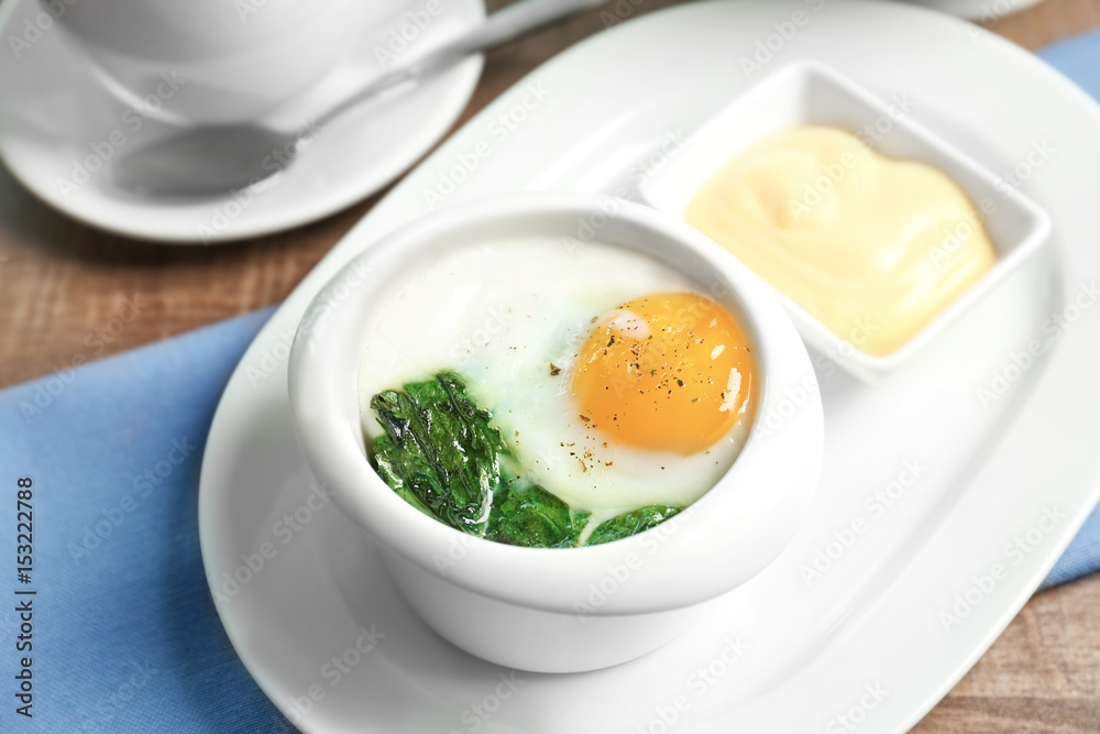 Plate with tasty egg and spinach on wooden table