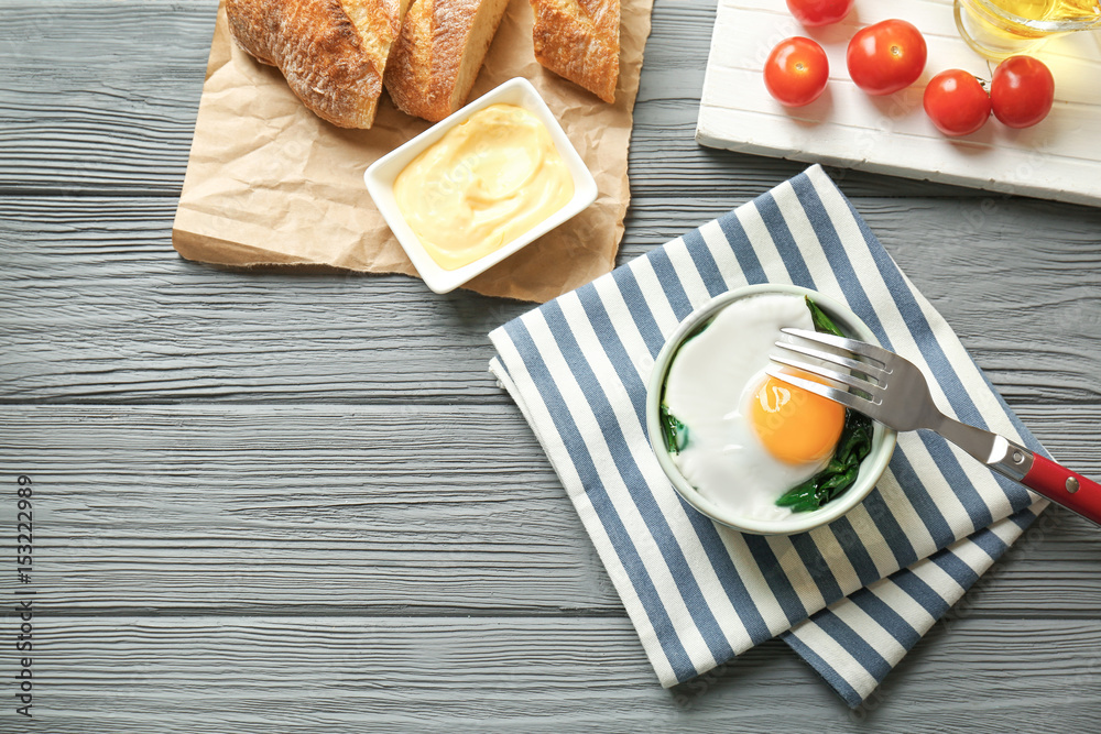 Bowl with tasty egg and spinach on wooden table