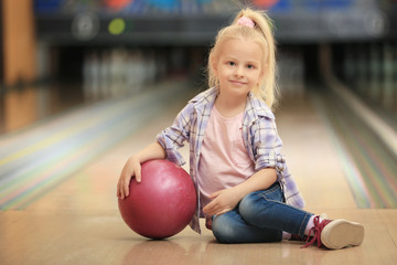 Wall Mural - Cute little girl with ball sitting on floor in bowling club