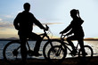 Image of sporty family on bicycles outdoors against sunset. Silhouette