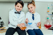 © LIGHTFIELD STUDIOS - Schoolchildren in white coats holding reagents in flasks sitting in science laboratory