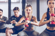 © LIGHTFIELD STUDIOS - group of athletic young people in sportswear with dumbbells squatting and exercising at the gym