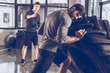 © LIGHTFIELD STUDIOS - side view of trainer helping man pulling tire while exercising at the gym
