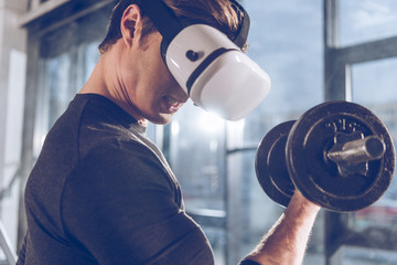 Wall Mural - side view of man in virtual reality headset exercising with dumbbell in gym