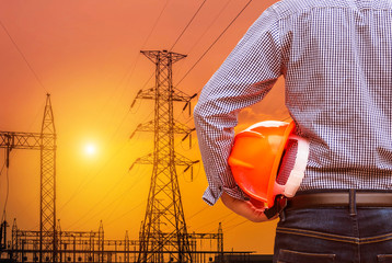 Canvas Print - engineer holding safety helmet with high voltage electric pillars substation on  sunset background  