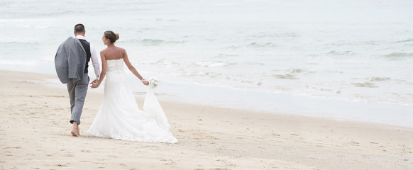 Wall Mural - Back view of bride and groom walking on the beach